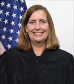 A smiling white woman with blonde hair wearing a judge&#039;s black robe.
