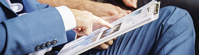 Close-up of a business person in a blue suit holding a clipboard in one hand and the other pointing to something on it